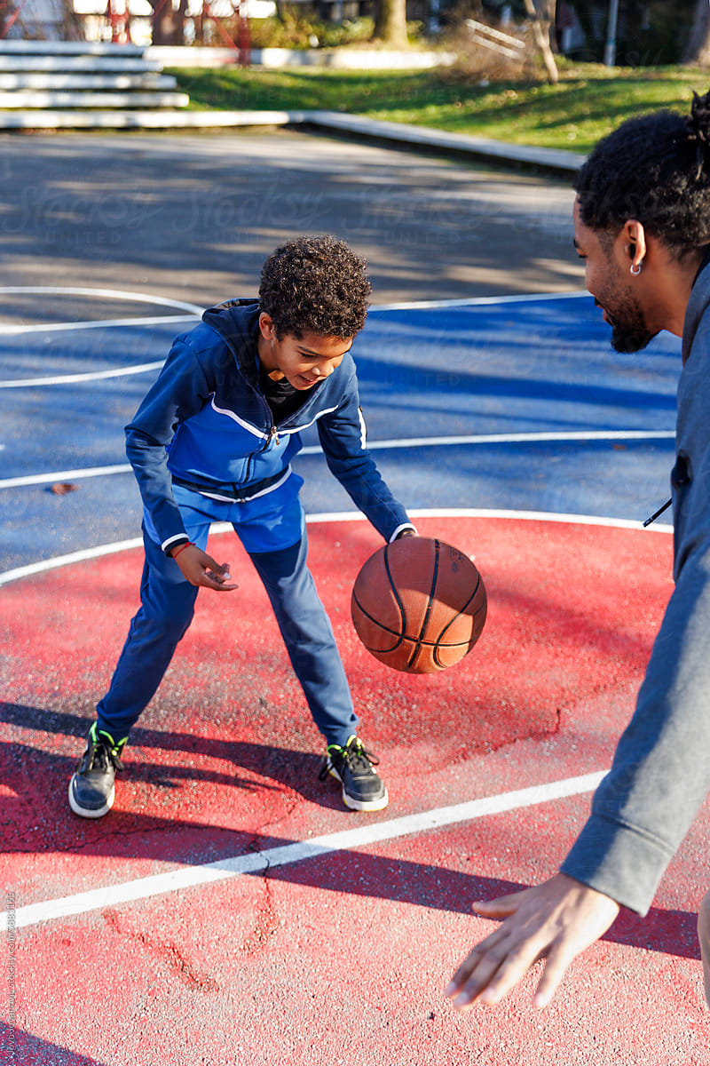Active boy learning dribbling basketball from father on court