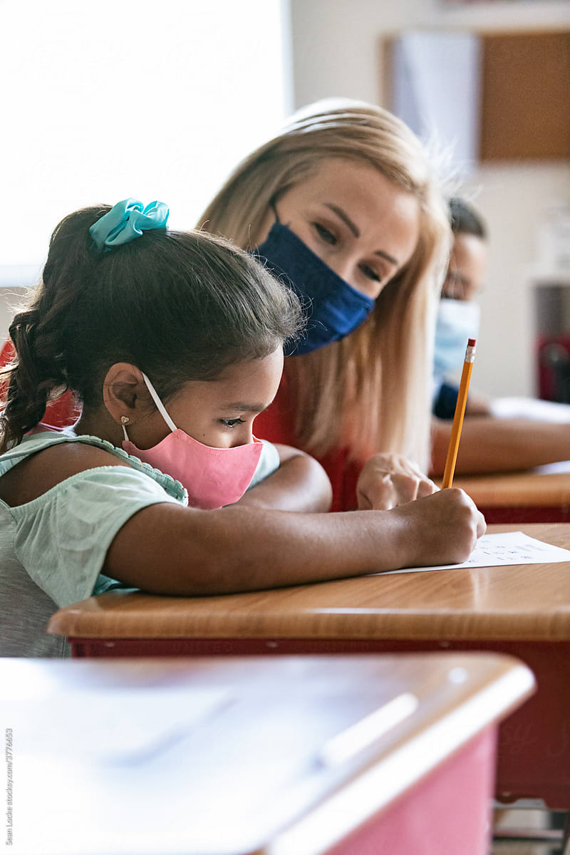 School: Teacher With Mask Helps Student With Math Sheet
