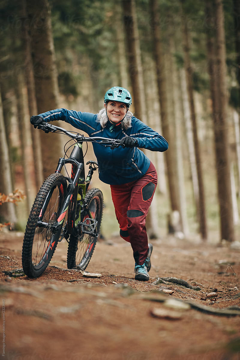 Mature woman pushing her mountain bike up a forest trail