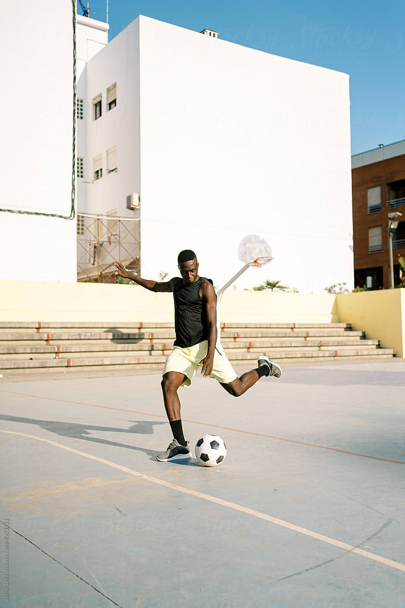 Black sportsman playing football on street
