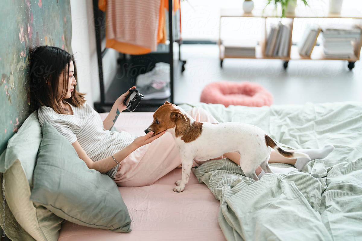 Woman with dog and smartphone chilling on bed