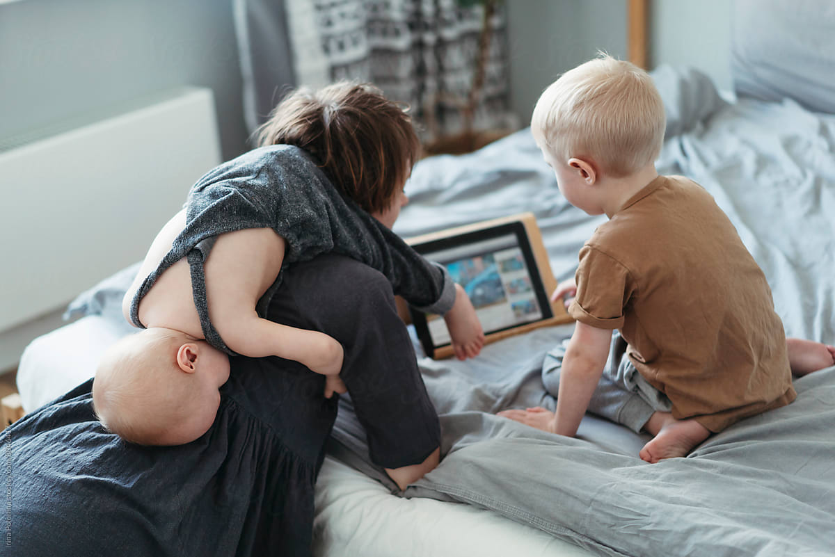 Young children play in an electronic tablet next to their mother.