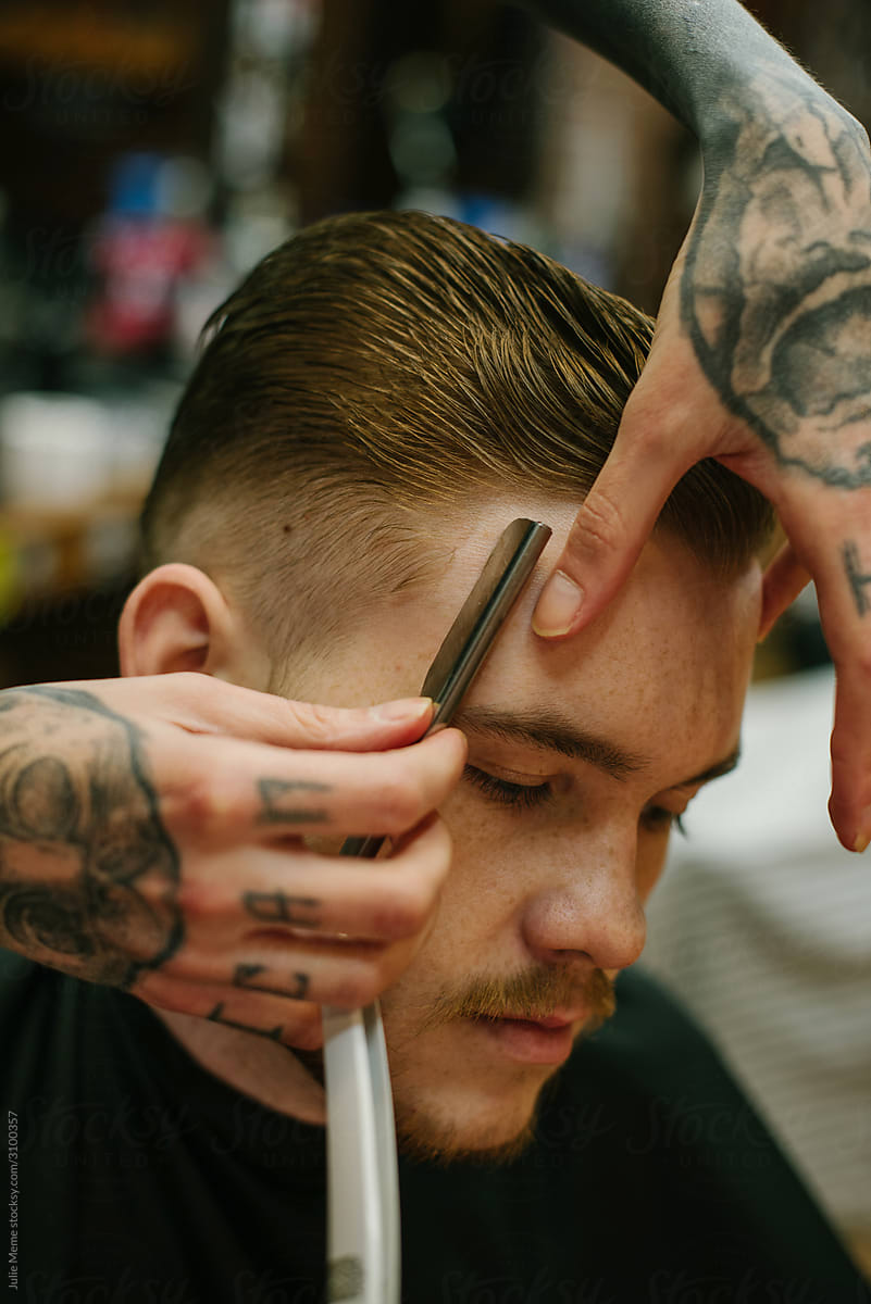 Closeup photo of a barber’s tattooed hands Shaving