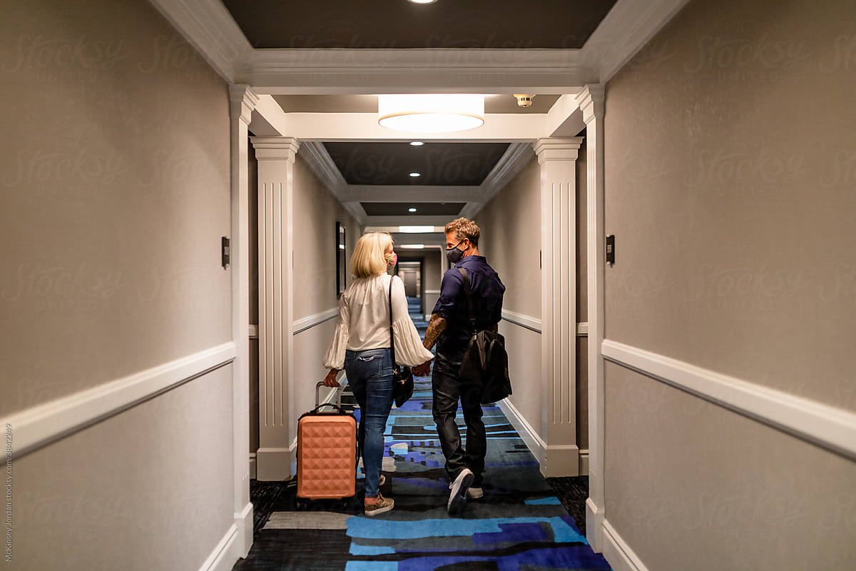 Couple Walks Down Hotel Hallway Wearing Masks