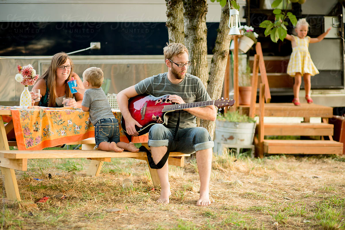 Young dad plays guitar with family outdoors