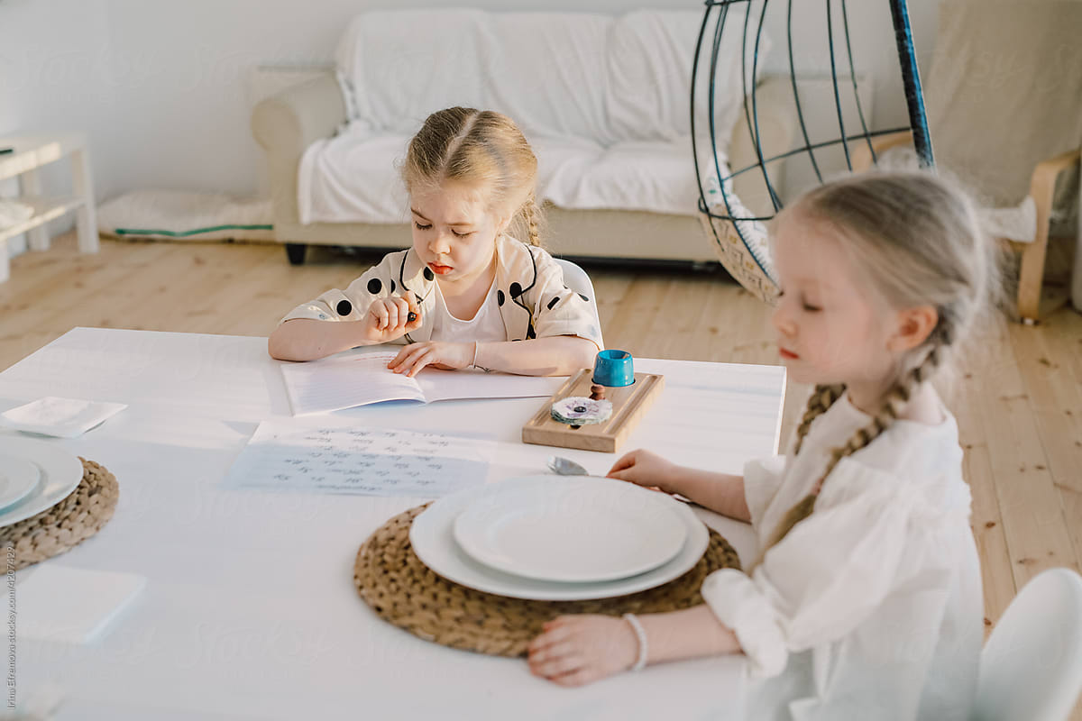 Girl practicing writing at the dining table next to her sister