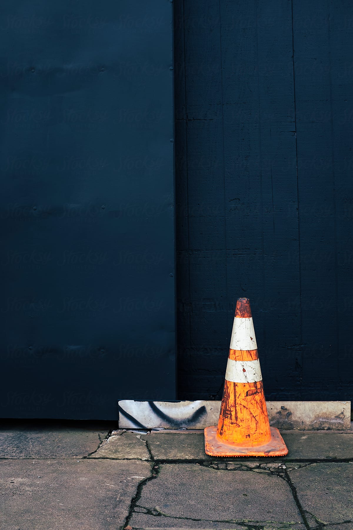 Traffic cone on cracked urban sidewalk, painted wall in background