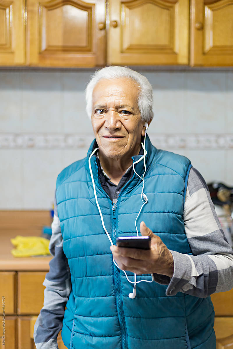 Portrait of elderly man looking at camera, using mobile phone