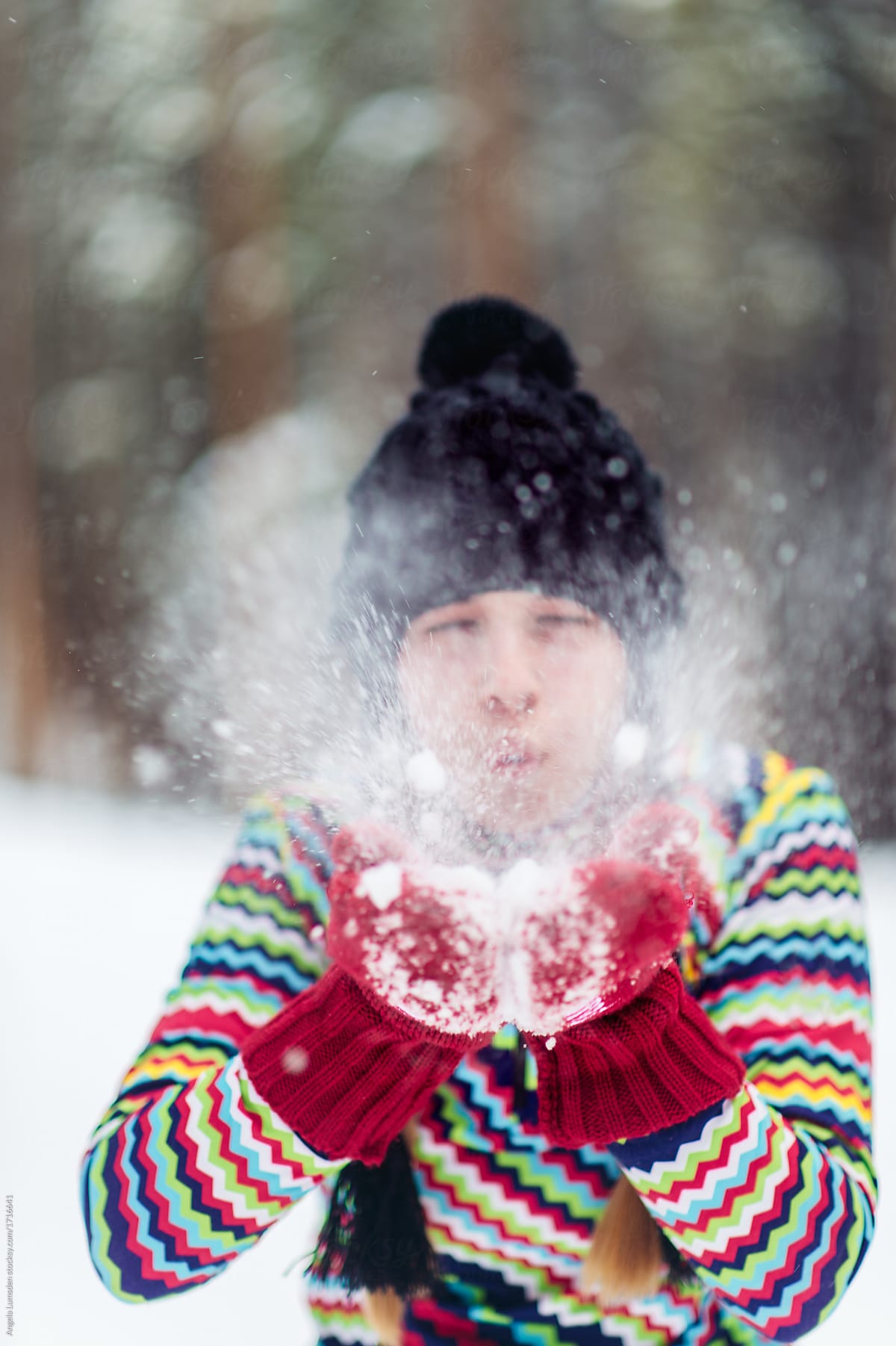 Teenage girl blowing snow out of red mittens in winter