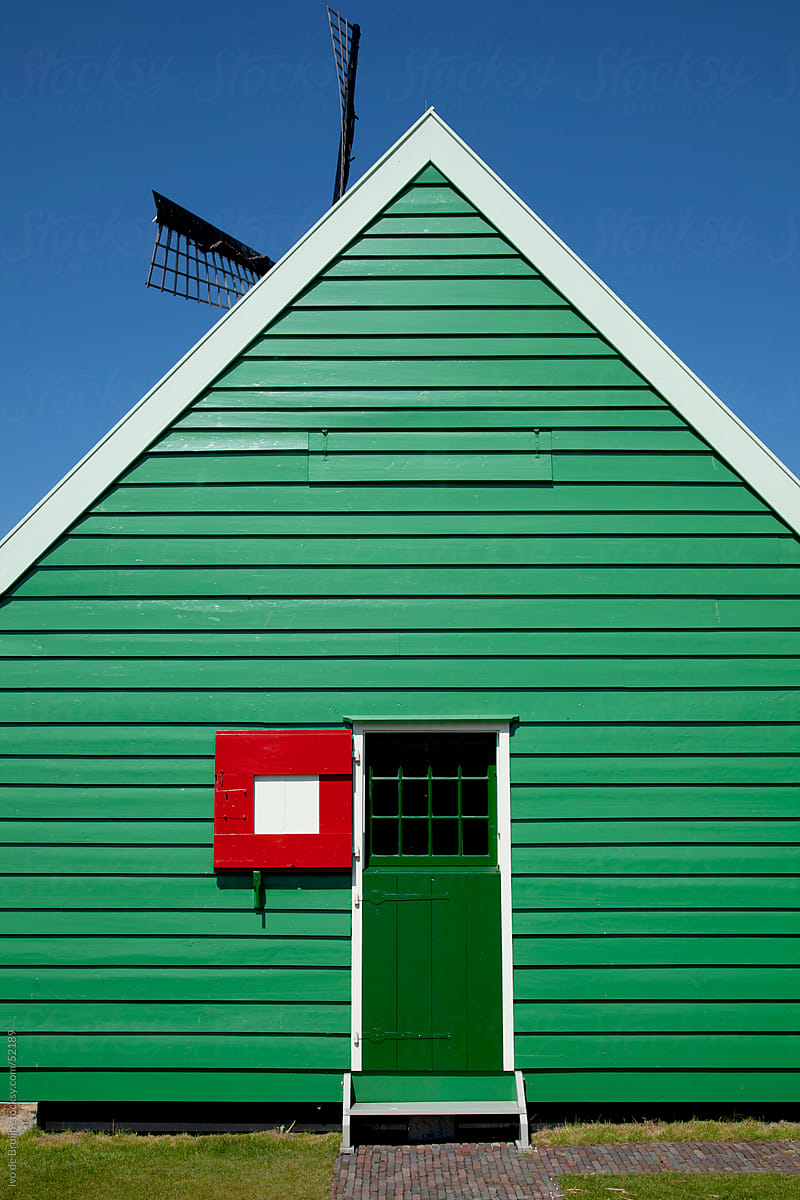 A green wooden house with a green door and a red shutter or hatch in the Netherlands
