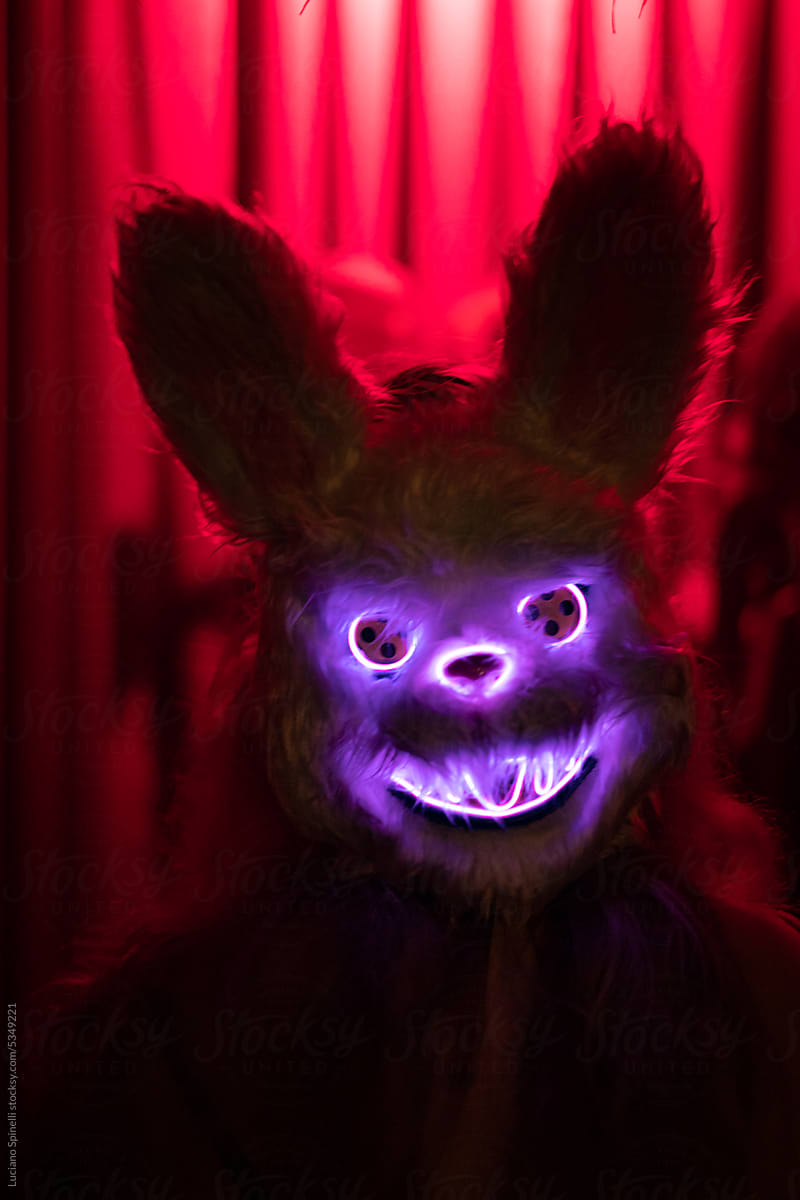 Person wearing a rabbit neon mask at dark easter halloween party