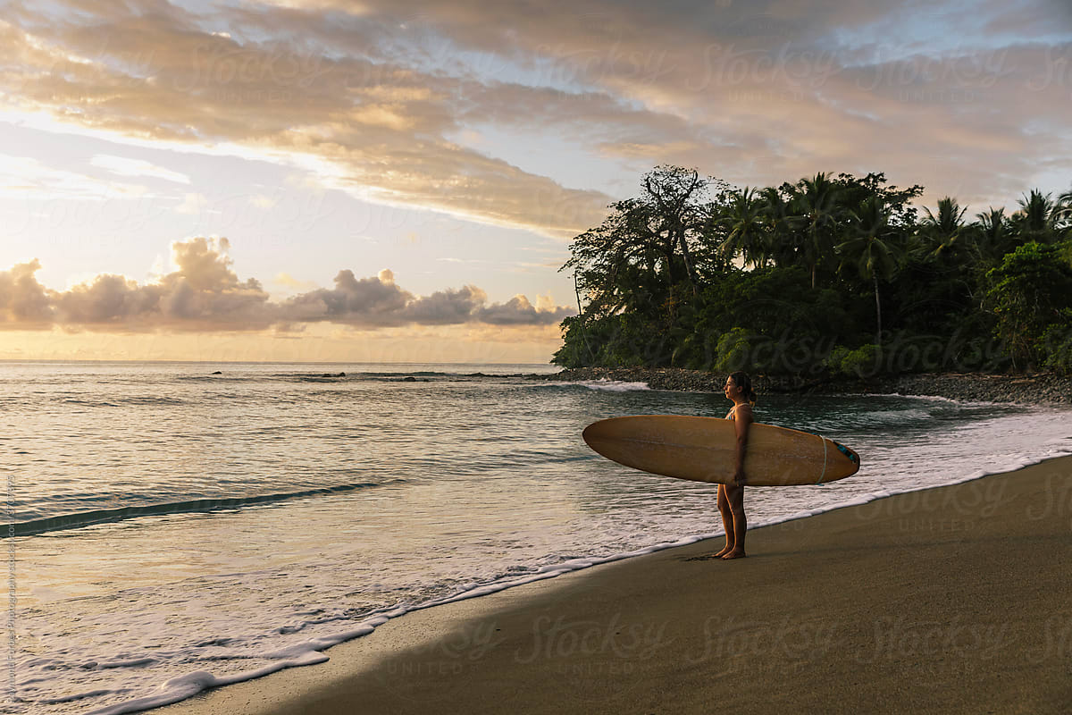 Female Surfer carries surfboard  in Costa Rica at sunrise