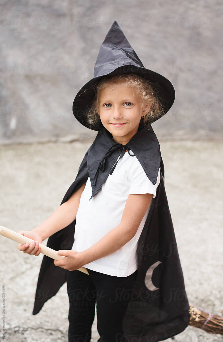 A little girl in a witch costume is playing outdoor.