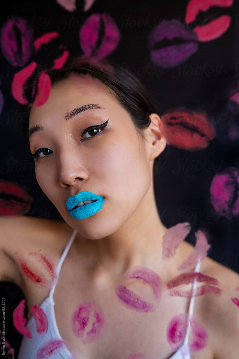 Woman with colorful makeup behind wall with kiss stains