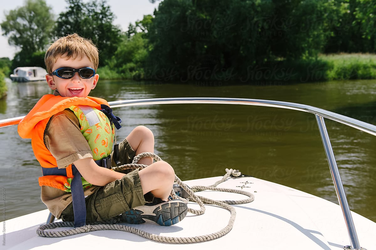 Happy child in life jacket sits on front of moving boat