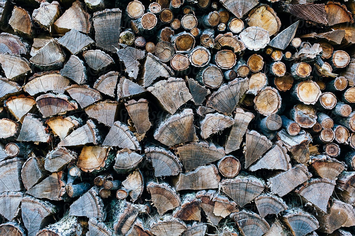 The ends of wooden logs in a large stack of firewood weathered by sitting outdoors.