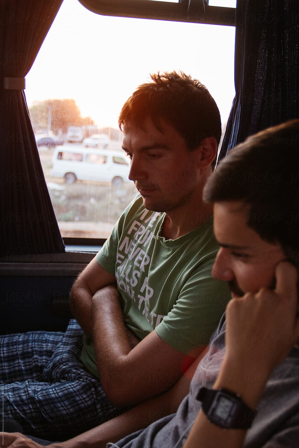 Two Young Men Traveling In A Bus At Sunset Watching A Movie On Their Laptop By Stocksy