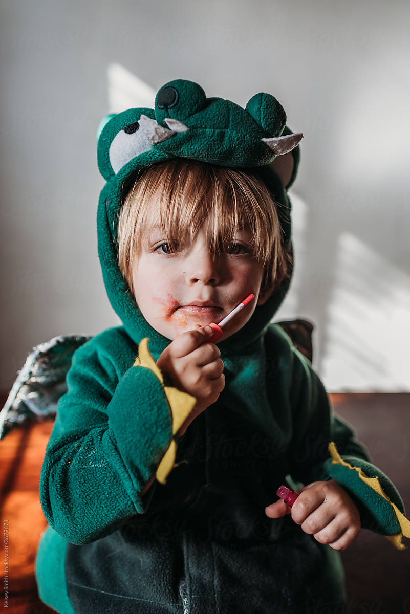 Toddler boy in dragon costume applies makeup at home