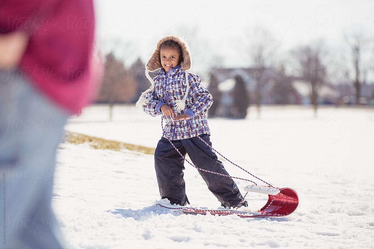 A child pulling her red toboggan up a snowy hill