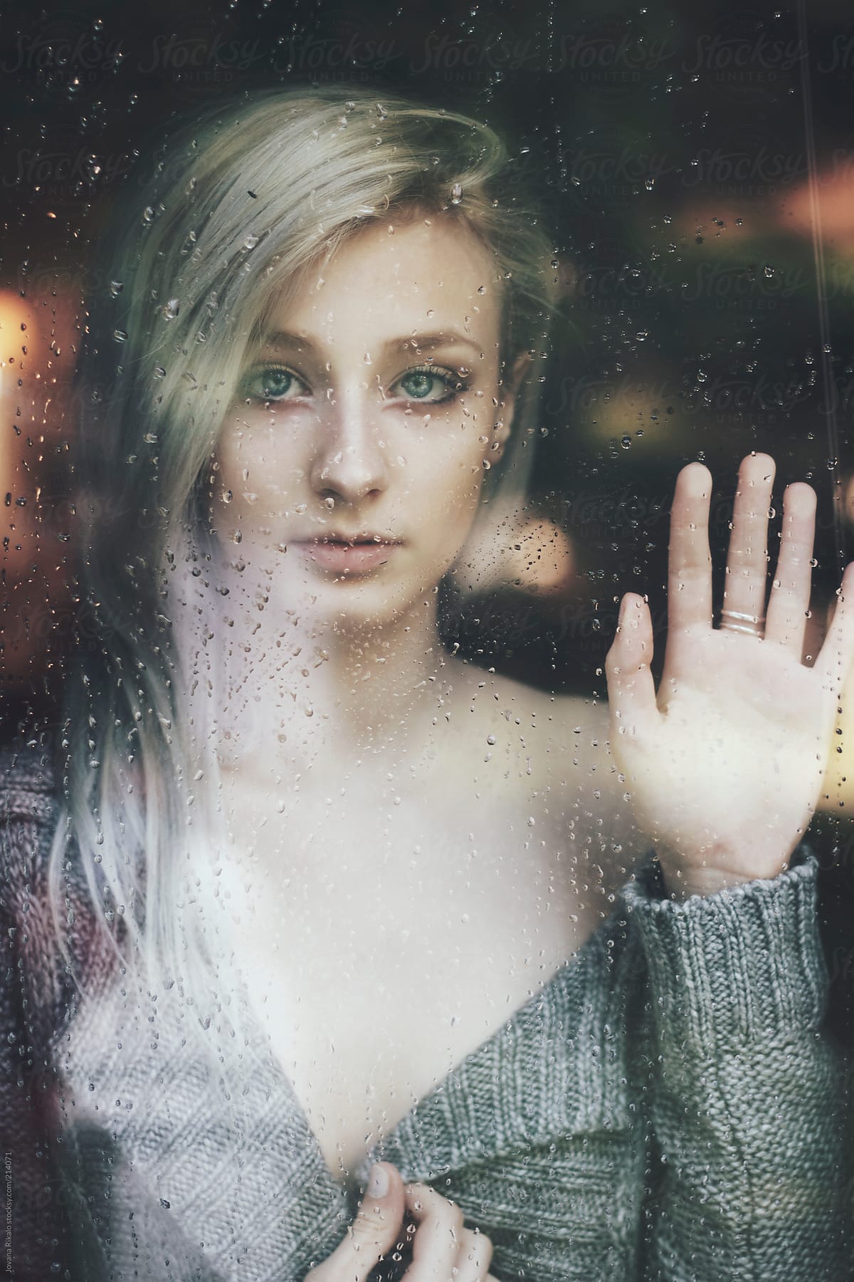 Beautiful young woman woman standing at the window watching the rain