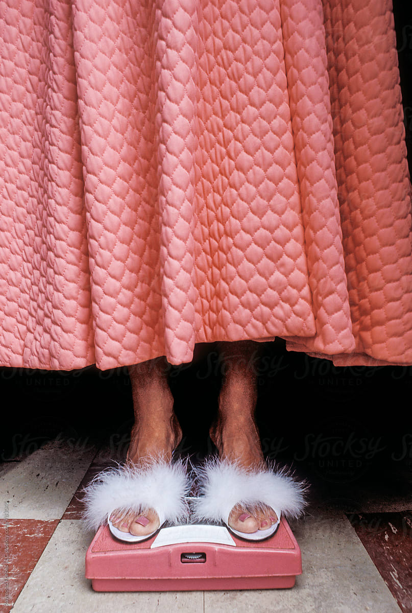 Woman In Pink Bathrobe On Bathroom Scale Furry Slippers by Stocksy  Contributor Raymond Forbes LLC - Stocksy