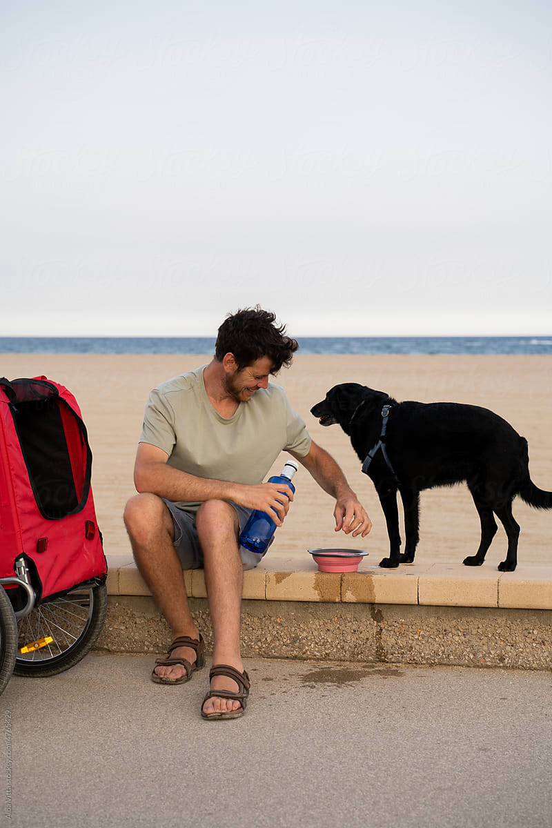 Man giving water do thirsty dog at beach