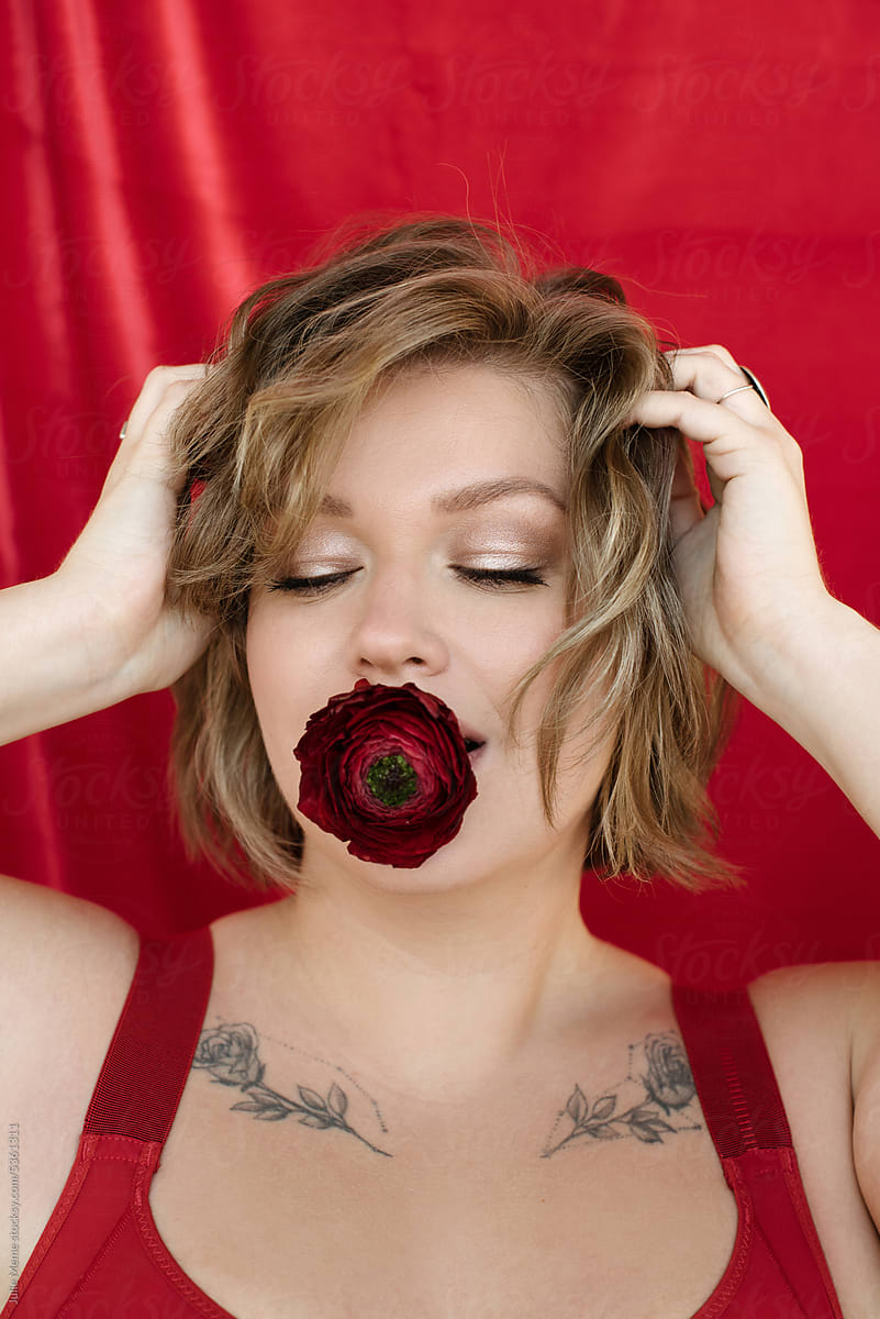 Young woman in red underwear and ranunculus in mouth