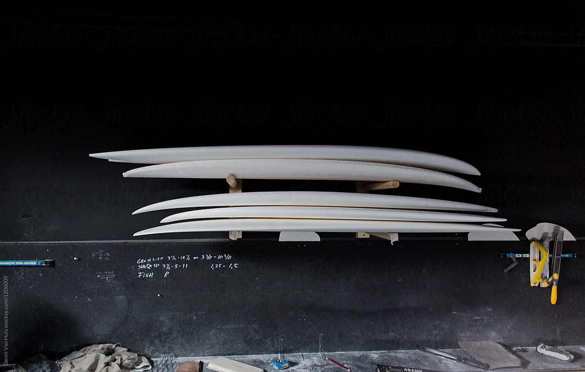 Surfboard stack in a shapers studio, piled up in front of a black wall.