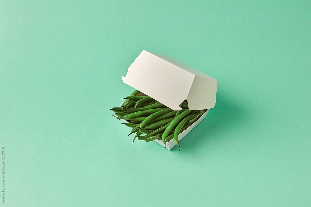 Paper lunch box with organic raw French beans on a green pastel