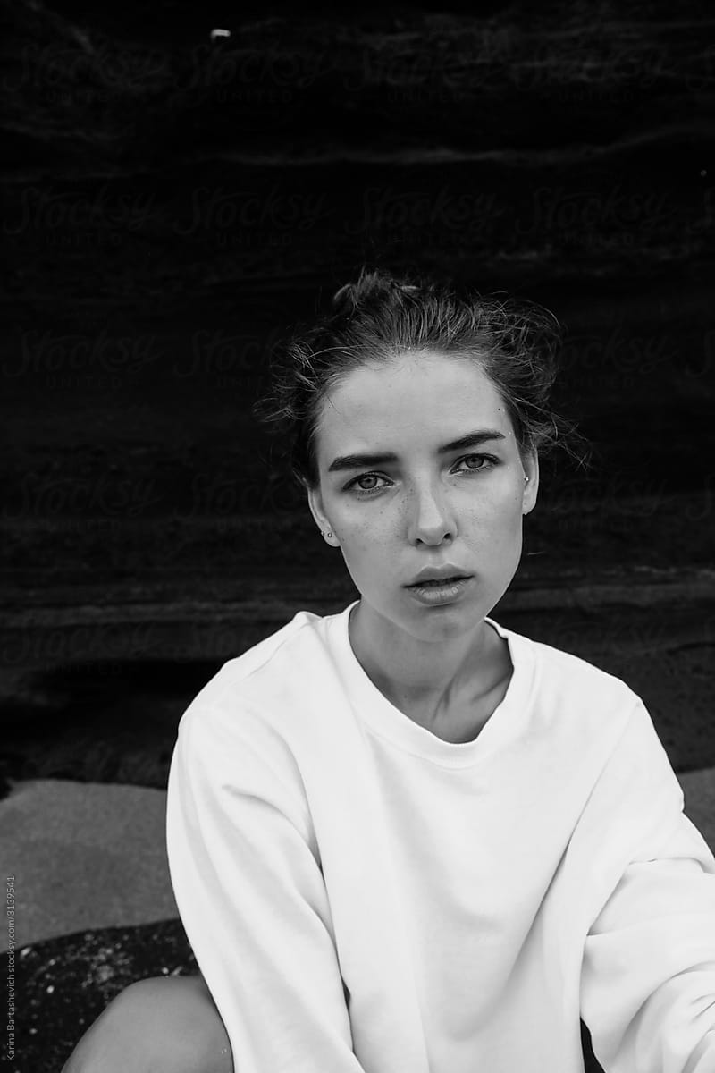black and white portrait of a girl in a white sweater with gathered hair looking at the camera on the beach