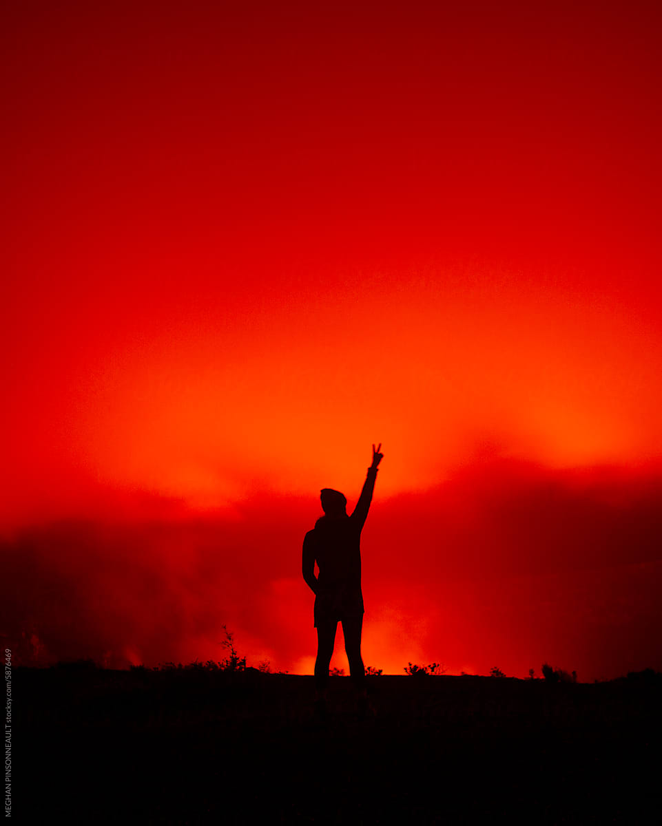 Silhouette of Woman Giving Peace Sign with Glow of Volcano at Night