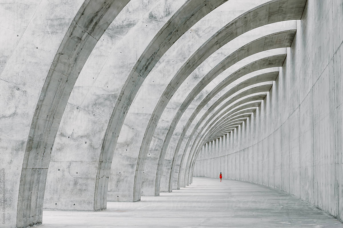 A girl dressed in red walks through concrete arches.