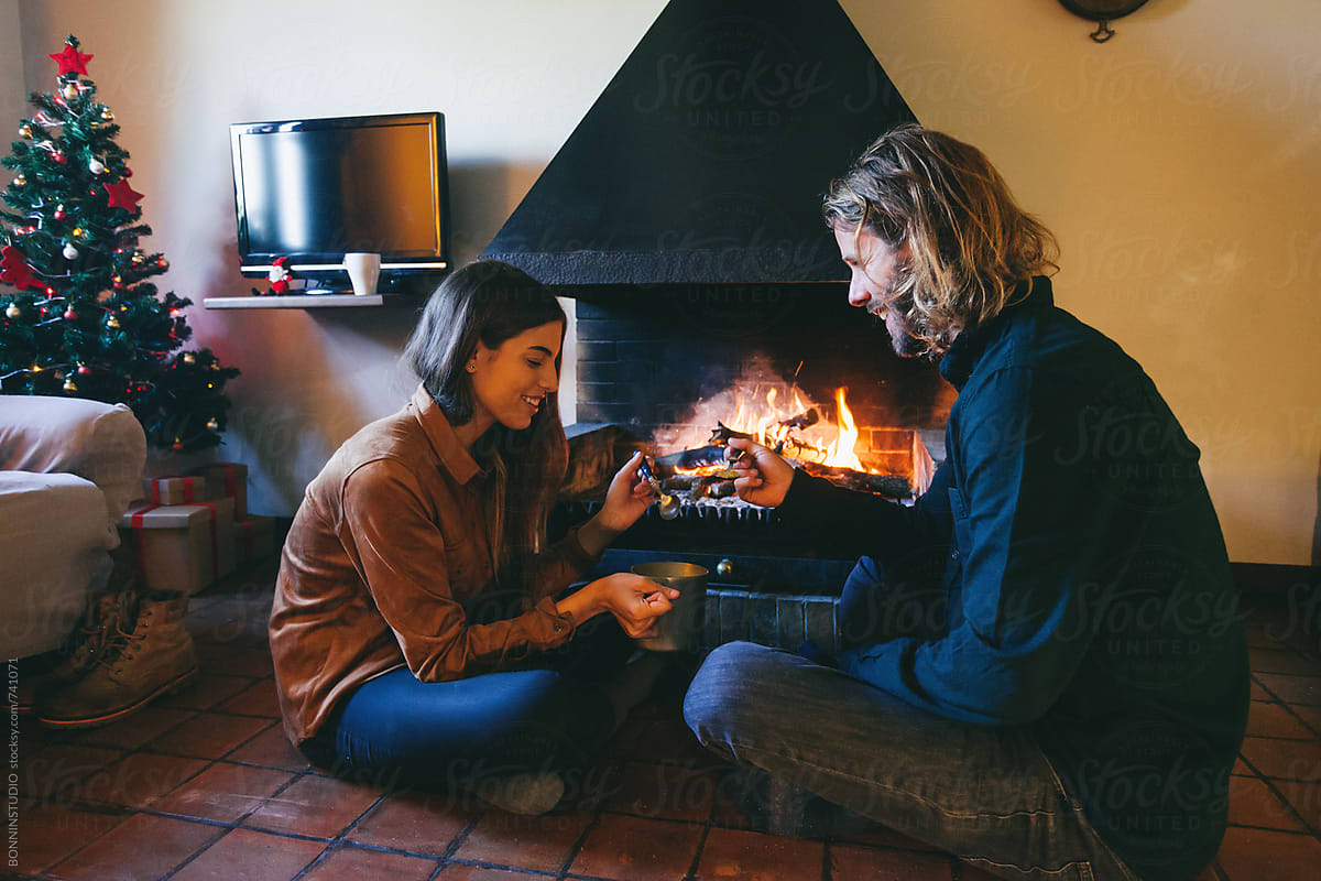 Couple eating a soup by the fireplace at home on winter.
