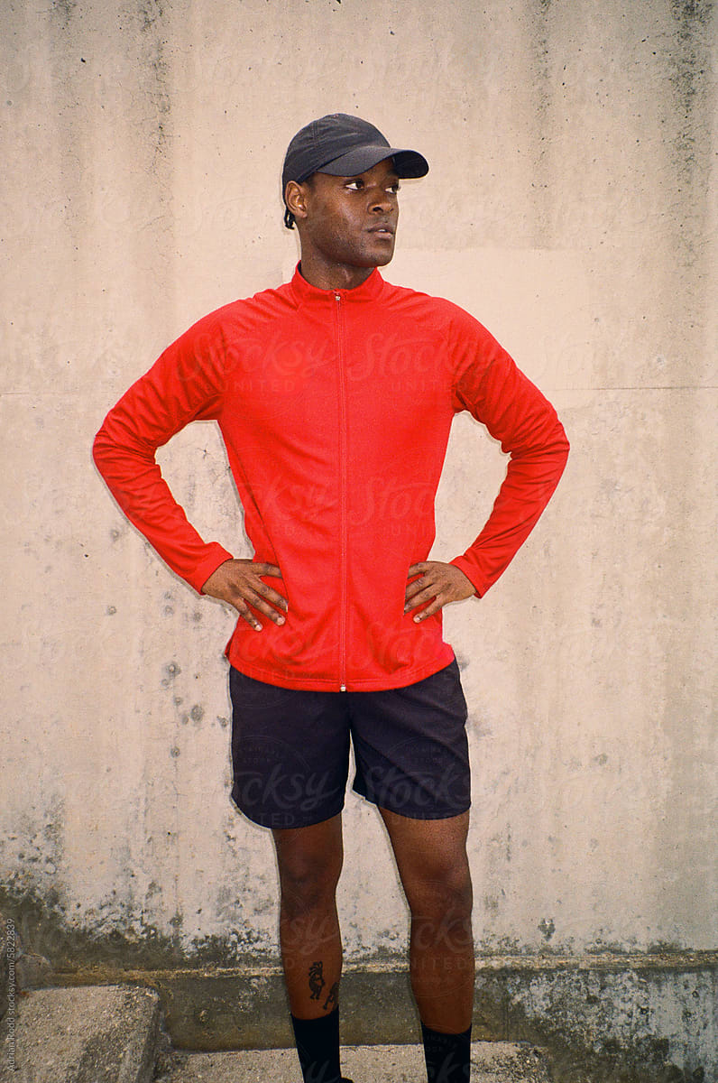 Film photo of black man donning a cap, shorts, and a red sports shirt