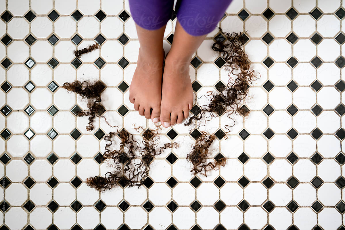 Feet on tile floor surrounded by cut hair