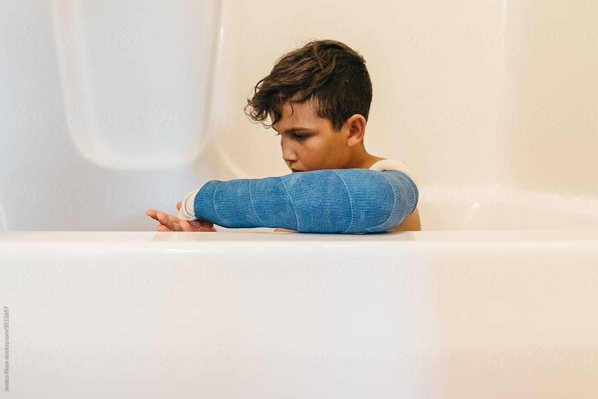 Boy with arm cast taking bath.