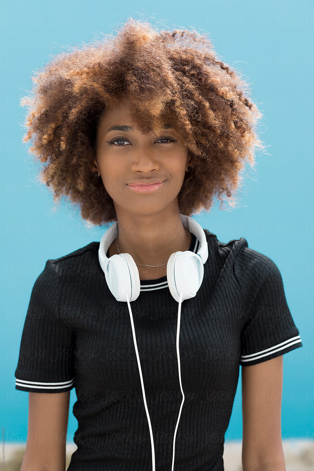 Young black woman with headphones and a blue wall.