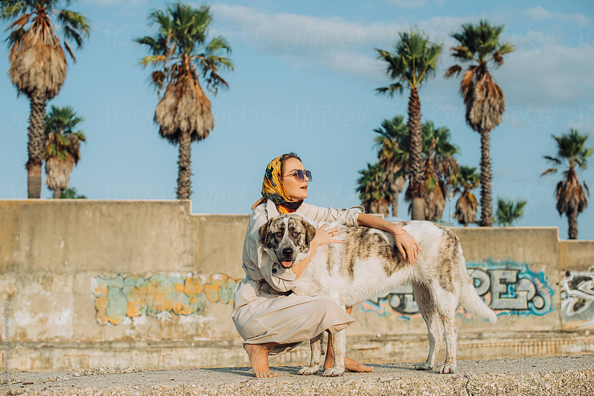 Woman hugging her dog with a wall and palm trees on background