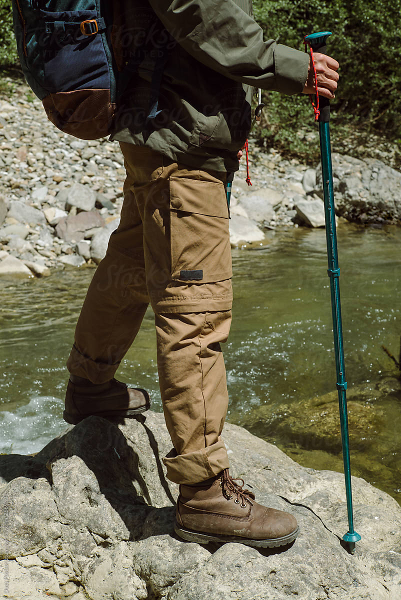 Woman with hiking poles. Trekking shoes on rocks and in runnig water.