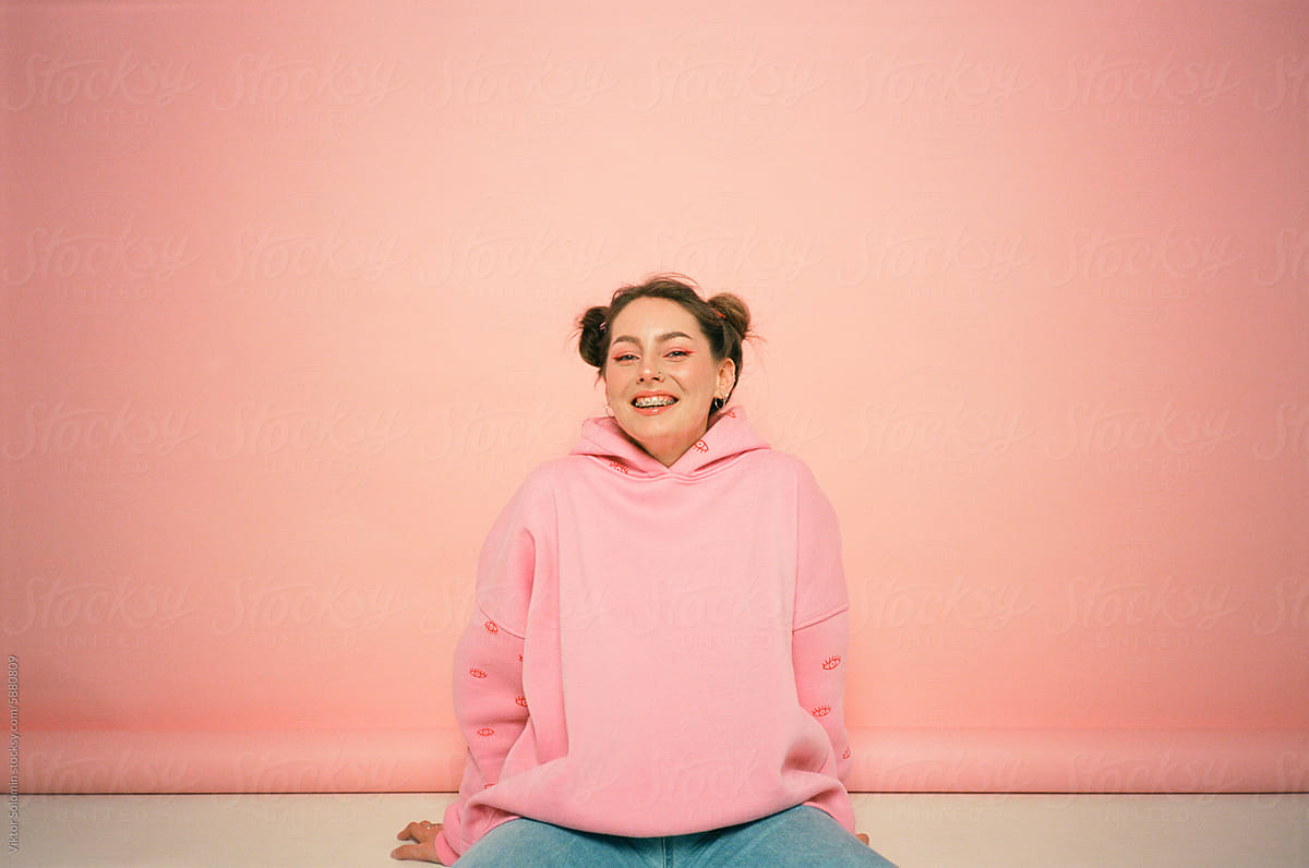 Cheerful woman in hoodie sitting floor on peachy background
