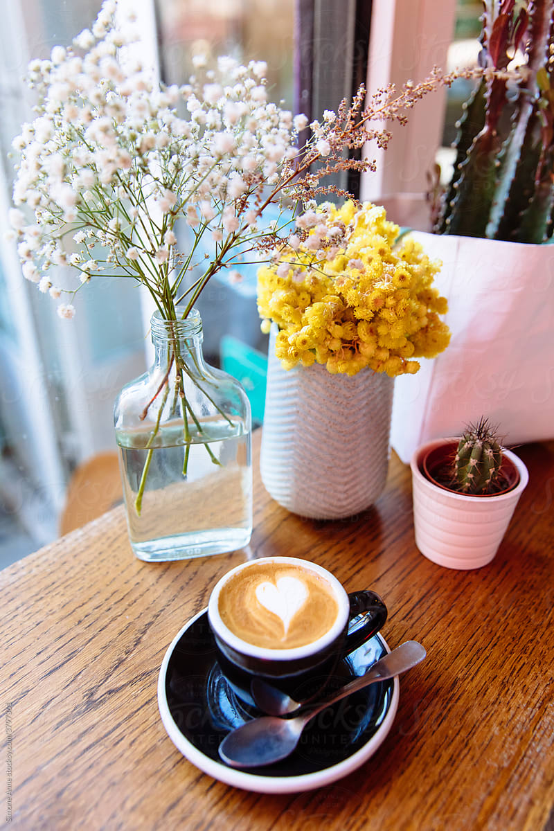 A cappuccino sits on a saucer on a wooden bar in a café with flowers