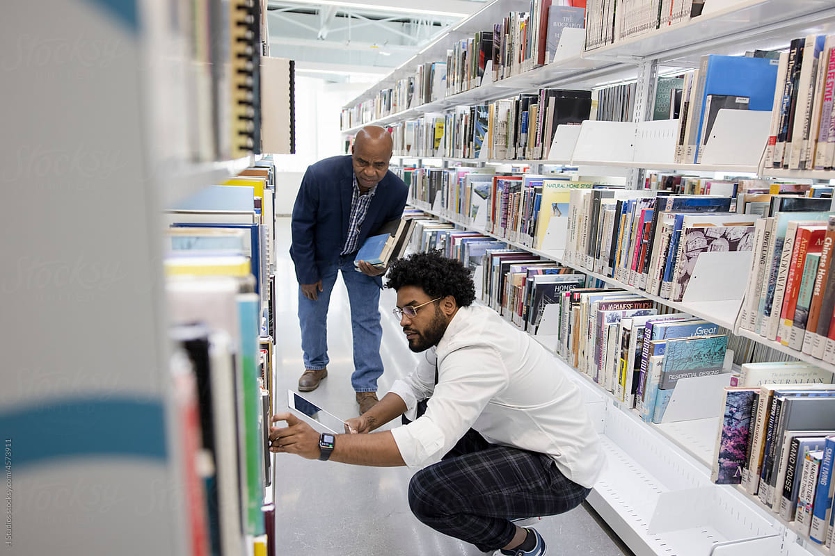 Librarian helping man find book on library bookshelf.