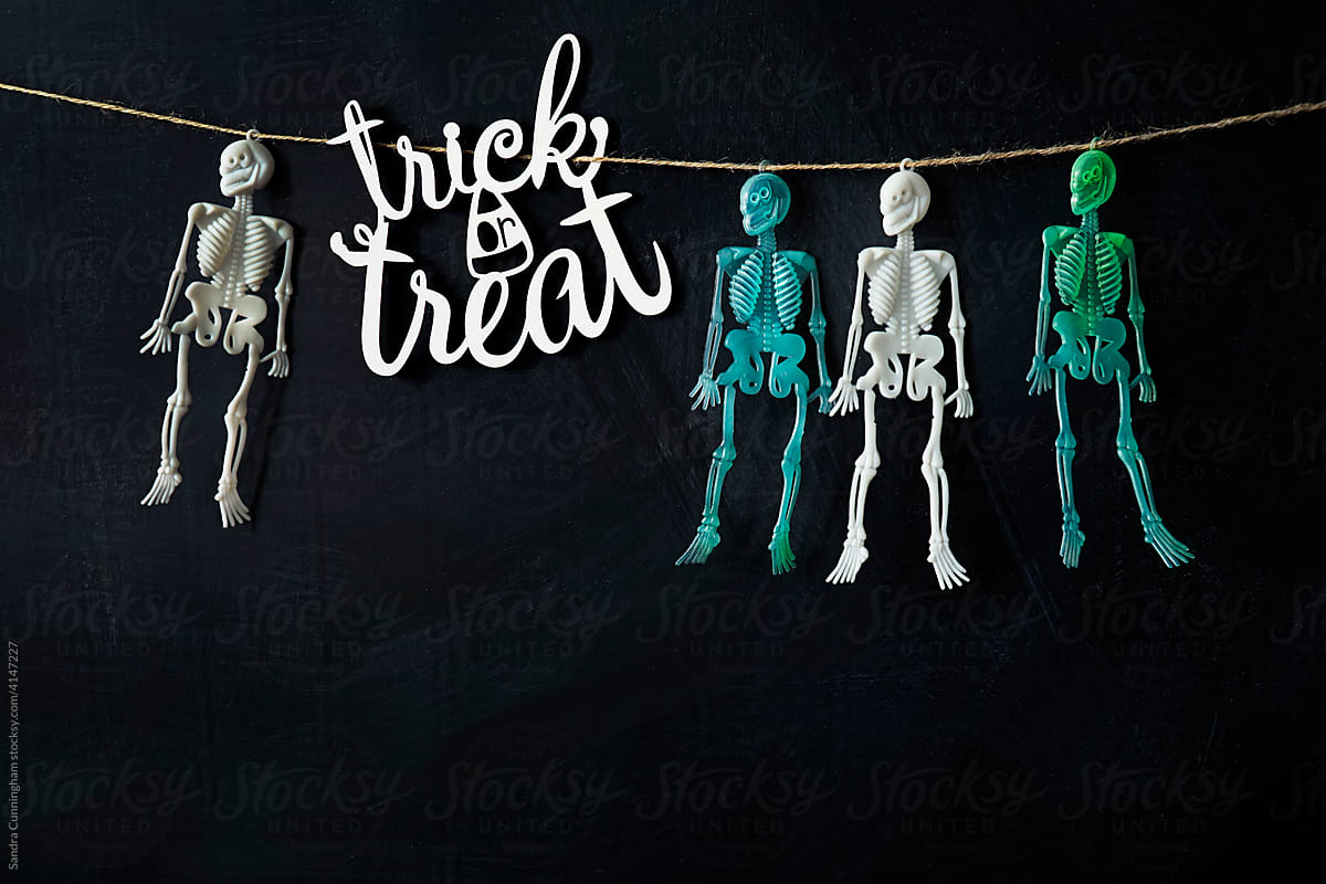 Trick or treat sign with four  skeletons hanging with string