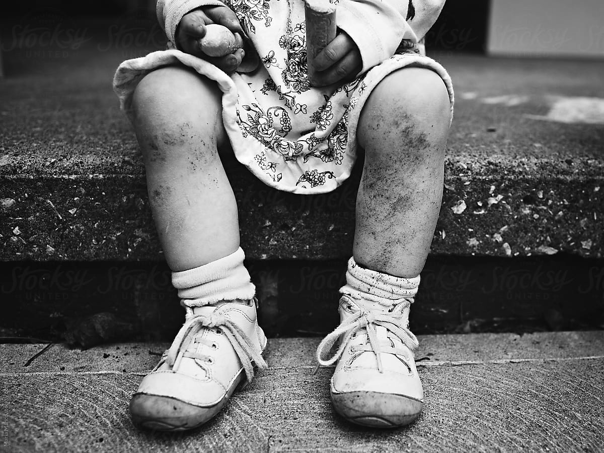 Little girl sits on step in a dress with dirt on her legs