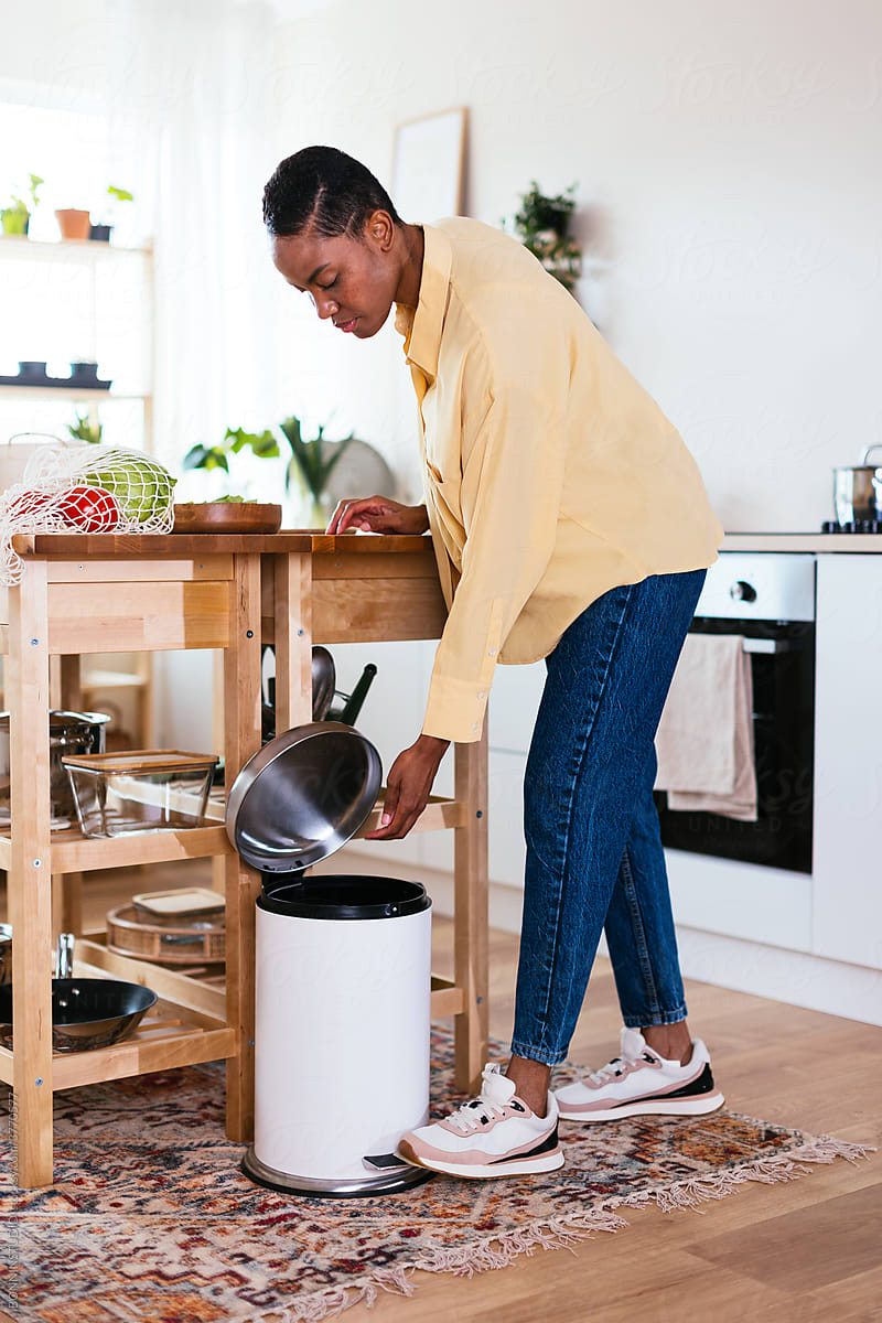 Black housewife dropping litter in bin in kitchen