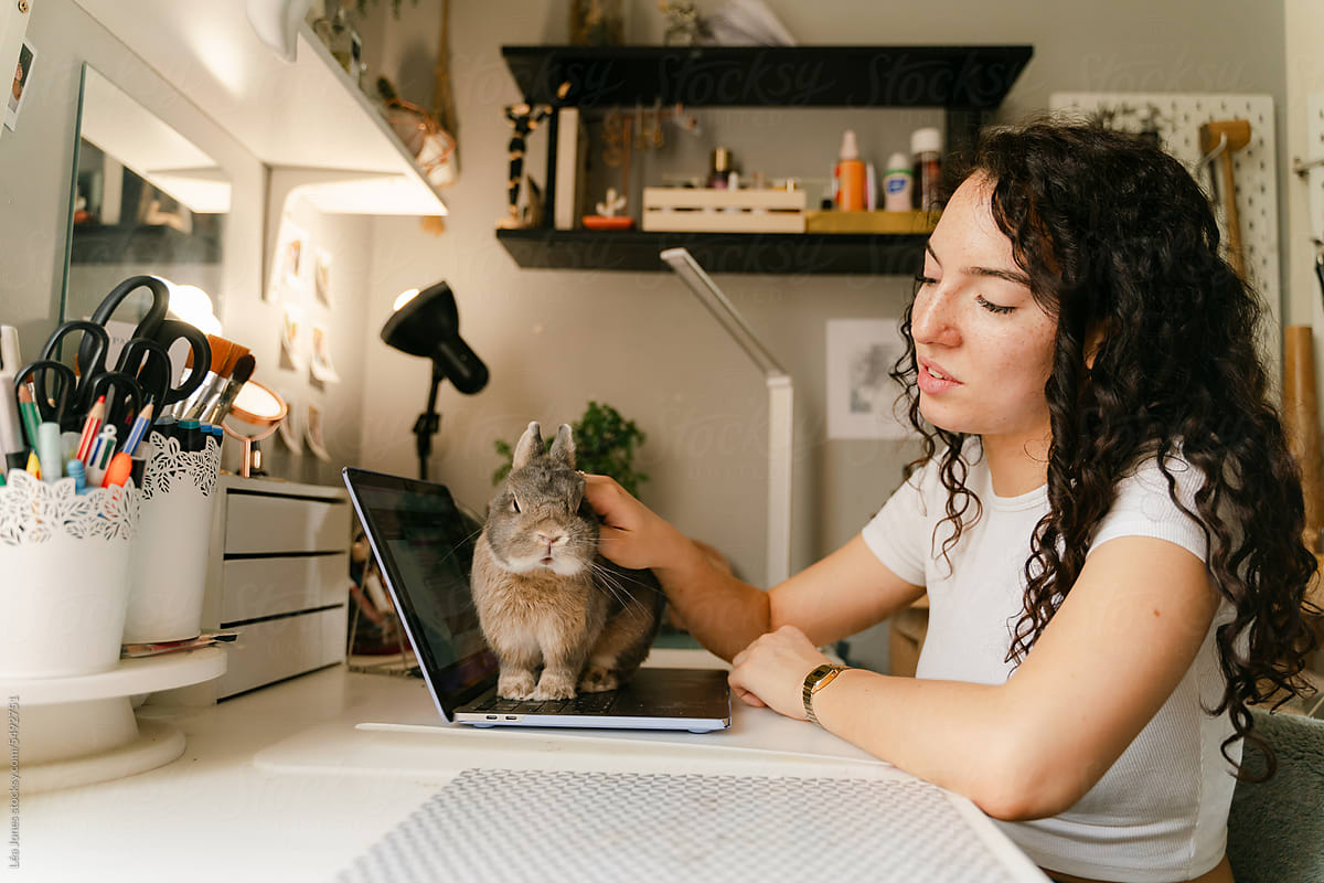 young student petting her adorable bunny sitting on her laptop