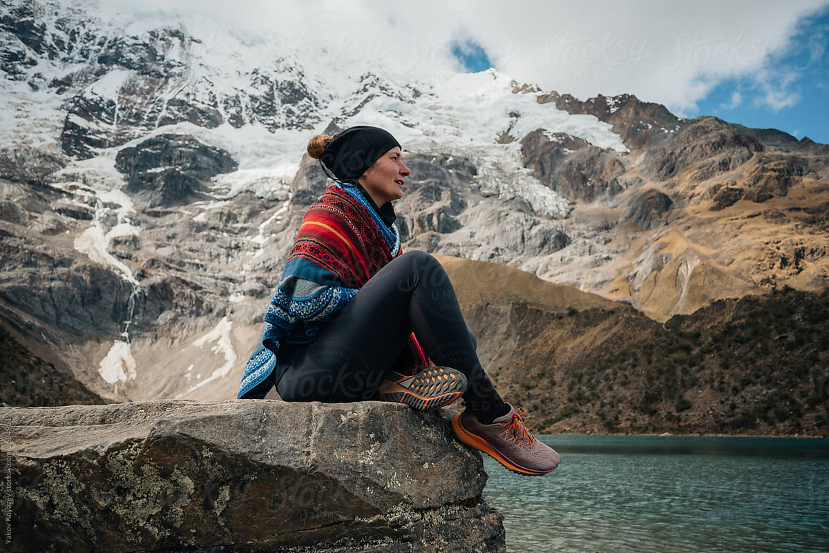 Woman sitting on a stone among Mountains wrapped in poncho