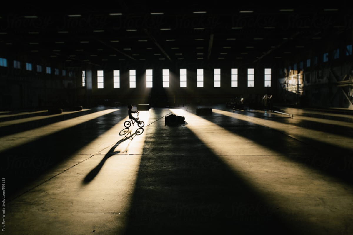 Child coasts on his bike, through a beam of light, casting a long shadow
