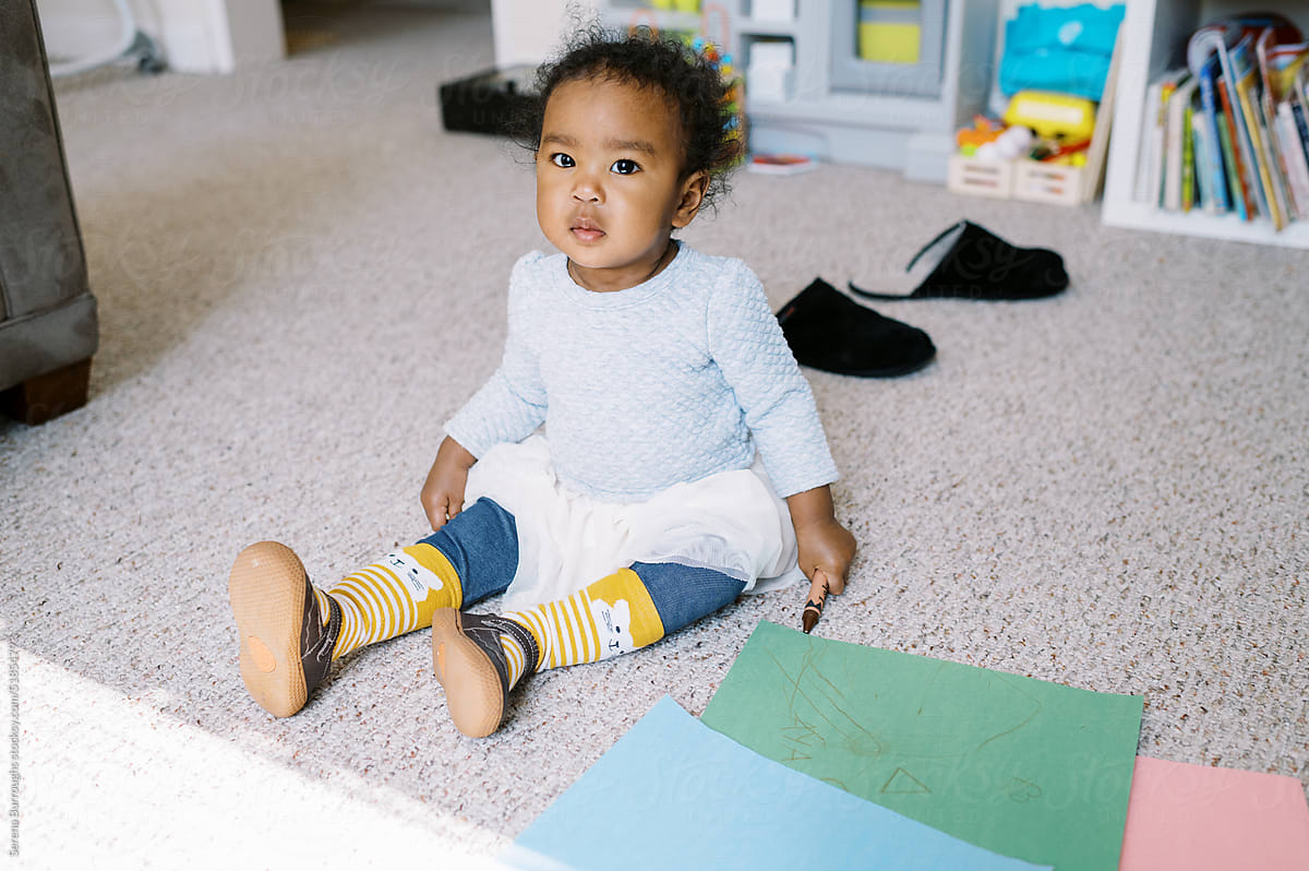 Beautiful multiracial baby sitting with a crayon in living room