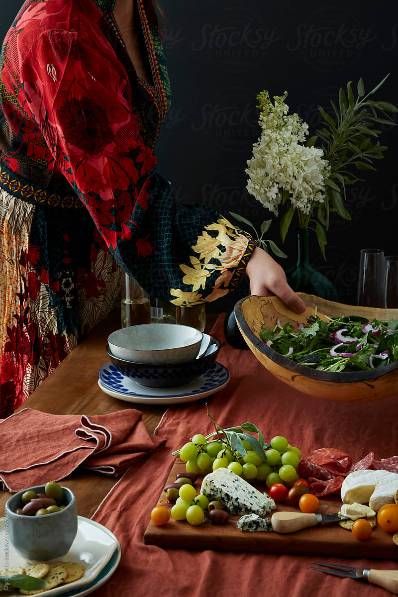 A woman in a patterned dress places a bowl of salad on a inner table